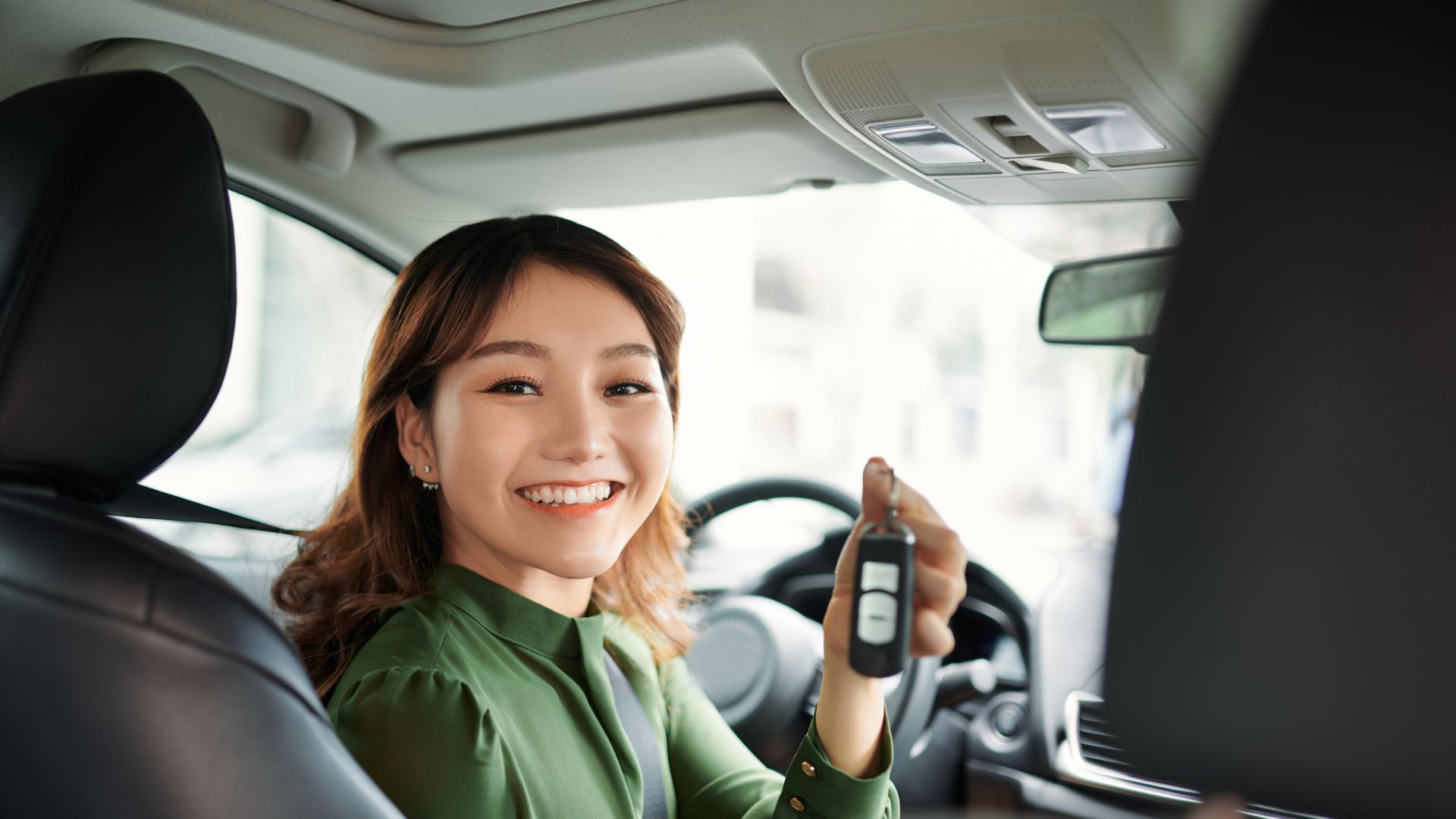 Smiling driver in green shirt holding car key inside vehicle