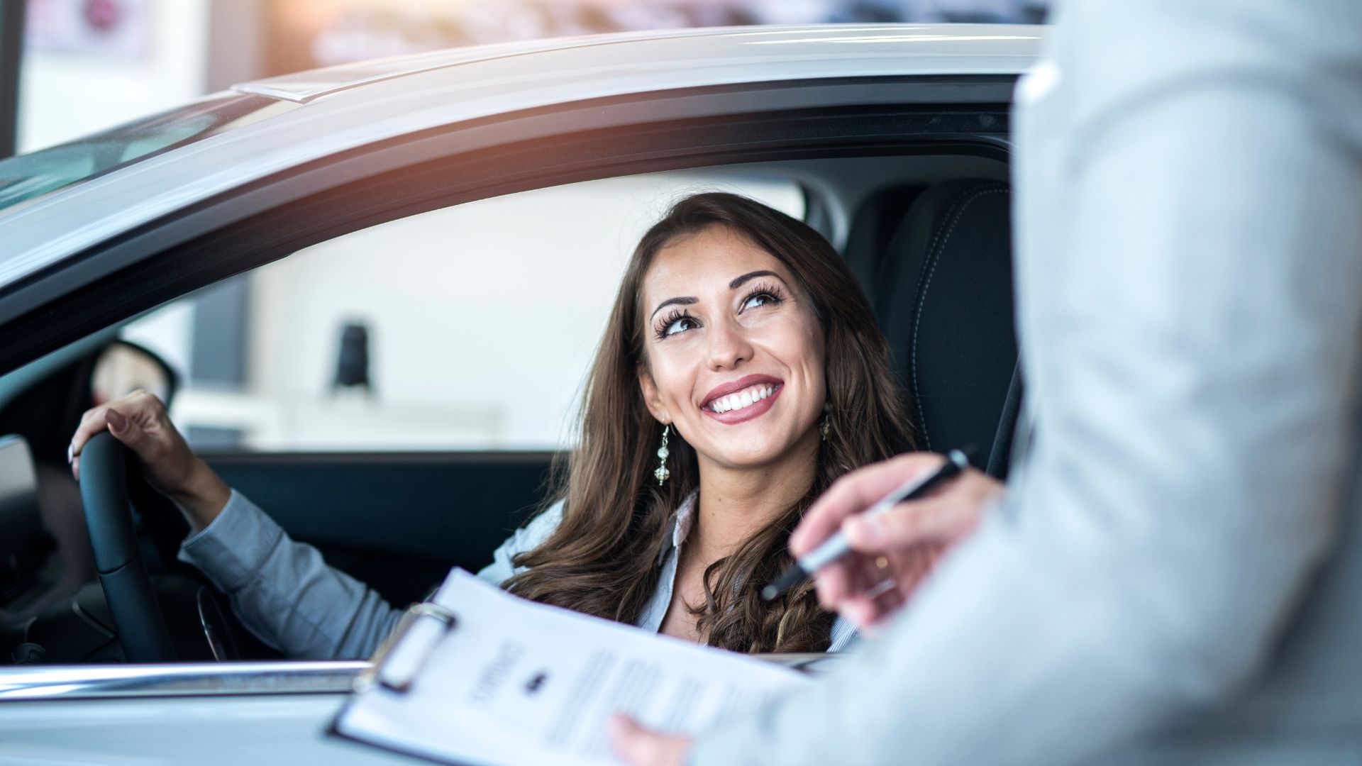 Smiling woman sitting in car during document signing at dealership