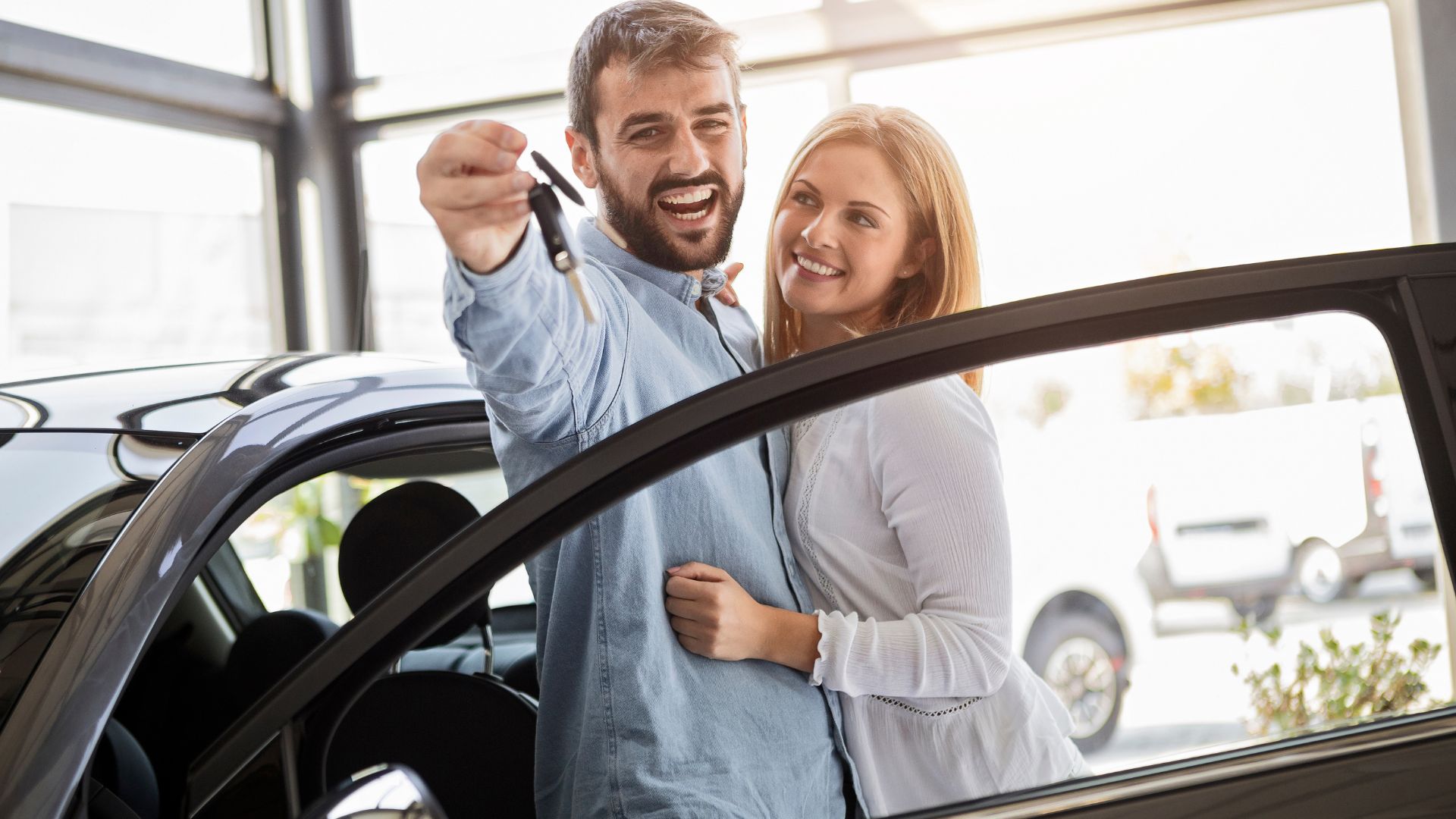 Excited couple holding car keys at dealership, celebrating new vehicle purchase