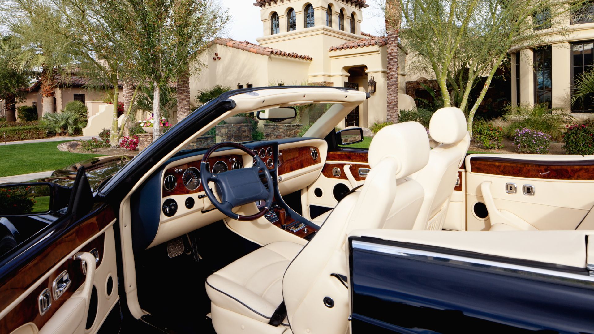 Luxury convertible with white leather interior parked in front of Mediterranean villa